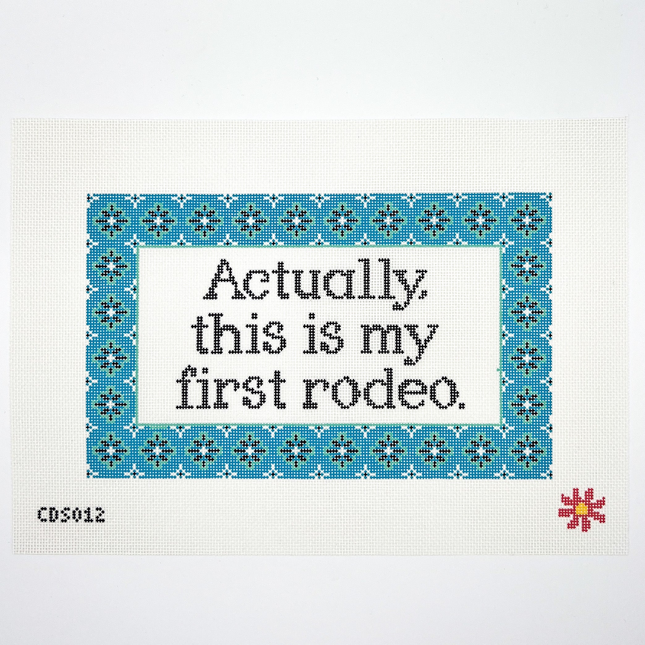 Needlepoint canvas with text on fabric with blue border and red flower, featuring the phrase &