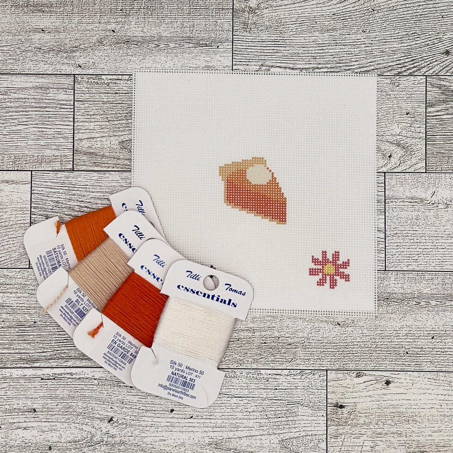 a cross-stitch pattern with a pie design, along with spools of thread in various colors and a small flower design.