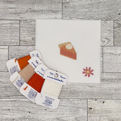 a cross-stitch pattern with a pie design, along with spools of thread in various colors and a small flower design.
