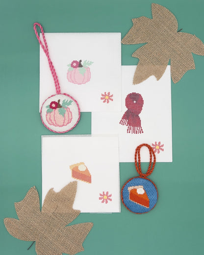 a collection of autumn-themed items, including a pumpkin-shaped ornament, a leaf-shaped ornament, and a pie-shaped ornament, all set against a green background.